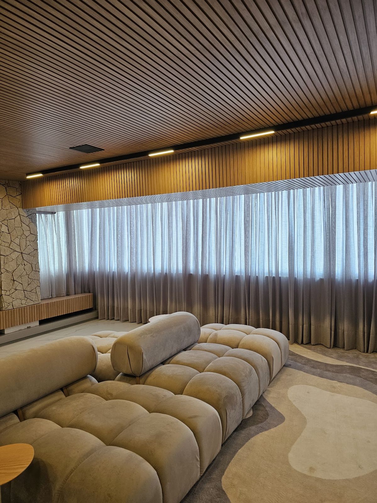Cortina de tecido instalada pela Homelux em living com painel de madeira
